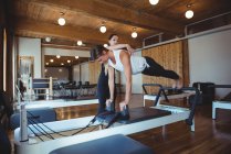 Entraîneur assistant une femme tout en pratiquant le pilates dans un studio de fitness — Photo de stock