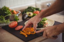 Primo piano delle mani maschili affettare il peperone sul tagliere in cucina — Foto stock