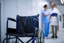 Пустое инвалидное кресло в коридоре больницы с врачами на заднем плане — стоковое фото