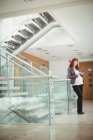 Grávida empresária usando telefone celular perto de escadas no escritório — Fotografia de Stock