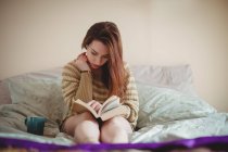 Женщина сидит на кровати и читает книгу дома — стоковое фото
