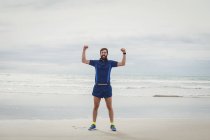 Portrait of athlete standing on beach with hands raised — Stock Photo