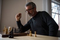 Внимательный человек играет в шахматы дома — стоковое фото