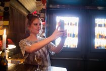 Красивая женщина делает селфи с мобильного телефона в баре — стоковое фото