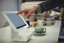 Mano dell'uomo utilizzando tablet digitale tenuto in stand in caffetteria — Foto stock