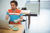 Homme utilisant un ordinateur portable tout en prenant une tasse de café dans un café — Photo de stock