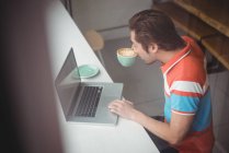 Uomo che utilizza il computer portatile mentre ha una tazza di caffè in caffetteria — Foto stock