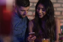 Smiling couple using mobile phone in bar — Stock Photo