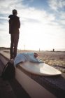Surfboard on beach with man standing in background — Stock Photo