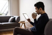 Homem usando tablet digital enquanto toma café em casa — Fotografia de Stock