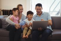 Sorrindo pais e filhos usando laptop na sala de estar em casa — Fotografia de Stock