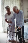 Partie médiane de la femme âgée aidant l'homme âgé à marcher avec marcheur à la maison — Photo de stock