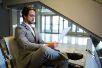Бизнесмен, сидящий со скрещенными ногами во время чтения газеты в зале ожидания — стоковое фото