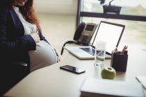 Беременная деловая женщина, трогающая живот в офисе — стоковое фото