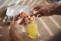 Close-up de mãos masculinas quebrando ovo em um copo na cozinha em casa — Fotografia de Stock