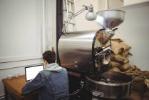 Man using laptop sitting besides coffee grinding machine in coffee shop — Stock Photo