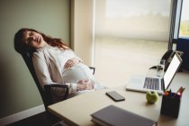 Беременная деловая женщина спит на стуле в офисе — стоковое фото
