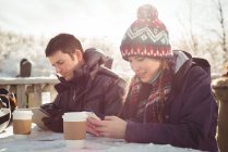 Happy skier couple using mobile phone and digital tablet at table in ski resort — Stock Photo