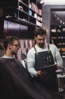 Peluquero mostrando el peinado al cliente en la tableta digital en la peluquería - foto de stock