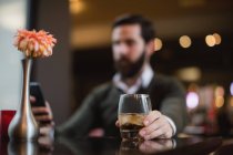Мужчина выпивает стакан во время использования мобильного телефона в баре — стоковое фото