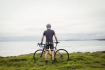 Спортсмен, стоячи з велосипеда на траві біля моря — стокове фото