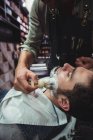 Парикмахер наносит крем на бороду клиента в парикмахерской — стоковое фото