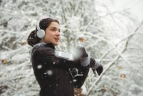Женщина слушает музыку в наушниках со смартфона зимой — стоковое фото