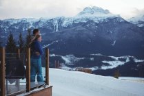 Couple embracing while standing by railing against snow capped mountains — Stock Photo
