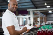 Retrato del trabajador masculino sonriente que observa productos en la fábrica de zumos - foto de stock
