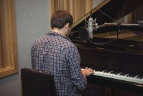 Vista trasera del hombre tocando un piano en un estudio de música - foto de stock