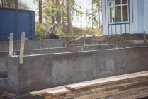 Concrete foundation and wooden planks at construction site, man working on background — Stock Photo
