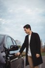 Mann öffnet Tür zu Elektroauto an Ladestation für Elektrofahrzeuge — Stockfoto