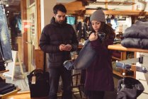 Жінка виборі одягу в магазині одягу під час людина за допомогою мобільного телефону — стокове фото