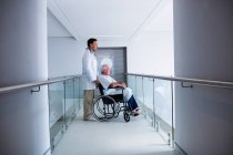 Médico de pie con un paciente mayor en una silla de ruedas en el hospital - foto de stock