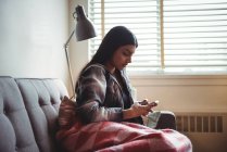 Woman using mobile phone while relaxing on sofa in living room at home — Stock Photo