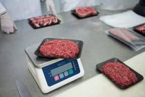Butcher weighing packages of minced meat at meat factory — Stock Photo