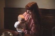 Мати тримає маленьку дитину в обіймах за столом кафе — стокове фото