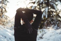 Visão traseira do homem esticando os braços na floresta durante o inverno — Fotografia de Stock