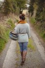 Вид ззаду жінки з кошиком, що йде по дорозі між полями — стокове фото