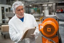 Trabajador serio inspeccionando máquinas en fábrica de bebidas frías - foto de stock