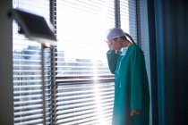 Cirujano hembra ensado de pie cerca de la ventana en el hospital - foto de stock
