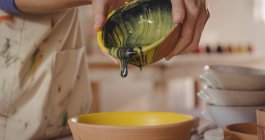 Gros plan du potier versant de l'aquarelle dans un bol dans un atelier de poterie — Photo de stock