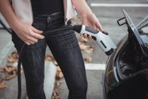 Средняя часть женщины заряжает электромобиль на улице — стоковое фото