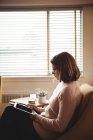 Женщина сидит на стуле с помощью цифрового планшета в гостиной на дому — стоковое фото