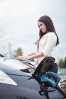 Beautiful woman using laptop while charging electric car on street — Stock Photo