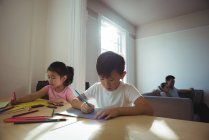 Boy and girl drawing in paper while parents using laptop in background at home — Stock Photo