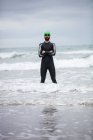 Atleta de terno molhado de pé com braços cruzados no mar na praia — Fotografia de Stock