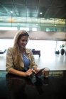 Усміхнена жінка використовує мобільний телефон в зоні очікування в терміналі аеропорту — стокове фото