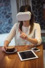 Бизнесвумен, сидя за столиком кафе с кофе, планшетом и телефоном, пользуется гарнитурой виртуальной реальности — стоковое фото