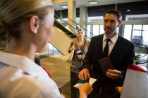 Female staff giving boarding pass to the businessman at the check in desk — Stock Photo